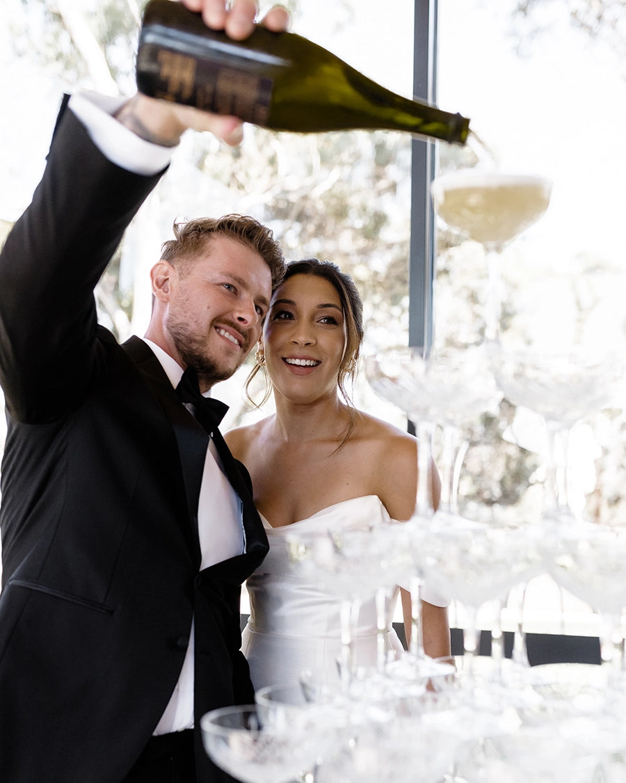 A bride and groom pouring champagne into a glass 